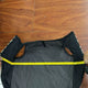 A black quilted garment is being measured with a yellow tape measure, stretched across its width, on a wooden floor.