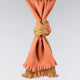A two-toned scarf, knotted neatly, features orange and brown sections with fringed edges, suspended against a plain light gray background.