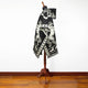 A black-and-white patterned cloak with horse designs drapes elegantly on a wooden mannequin, set against a plain white wall and hardwood floor.
