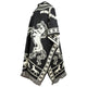 A poncho displays an elaborate white horse design on a black background, with geometric patterns. It drapes elegantly, featuring fringed edges, conveying a rustic and traditional aesthetic.