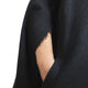 A black, fringed fabric drapes over an arm, revealing skin through a sleeve opening, against a plain background.