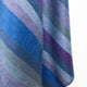 Morona baby alpaca wool blanket – a woven fabric showcases diagonal stripes in shades of blue, purple, and gray, hanging smoothly. The background is plain and light, highlighting the fabric's soft texture