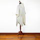 A white shawl drapes over a wooden mannequin stand, set against a plain white wall and a polished wooden floor.