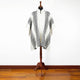 A black and white patterned poncho is displayed on a wooden mannequin stand, set against a plain white wall and hardwood floor.