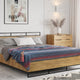Huasaga baby alpaca wool blanket – a wooden bed with gray and white pillows and a striped blanket sits in a bedroom. A dresser and Paris-themed artwork decorate the brick-wall setting