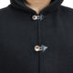 A person wears a dark hooded coat, fastened with two looped buttons, against a plain background.