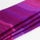 Chone baby alpaca wool blanket – a folded, multicolored woolen fabric lies neatly with shades of purple, pink, and red, creating horizontal stripes. The setting is plain, emphasizing the vibrant textile