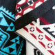 Textile fabric displays geometric patterns, featuring blue and red designs. The material appears draped, showcasing intricate triangular and zigzag motifs against black, white, and cream backgrounds.