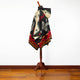 A poncho with geometric patterns in black, red, and cream drapes over a wooden stand, set against a white wall and wooden floor.