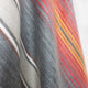 Ajilanga baby alpaca wool blanket – a close-up view of a fabric featuring diagonal stripes in orange, yellow, pink, gray, brown, and cream, creating a layered appearance with a soft texture