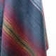 Huasaga baby alpaca wool blanket – a woolen fabric displays gradient stripes of red, yellow, and blue, creating a smooth texture and rich color transition. The fabric hangs against a plain, light background
