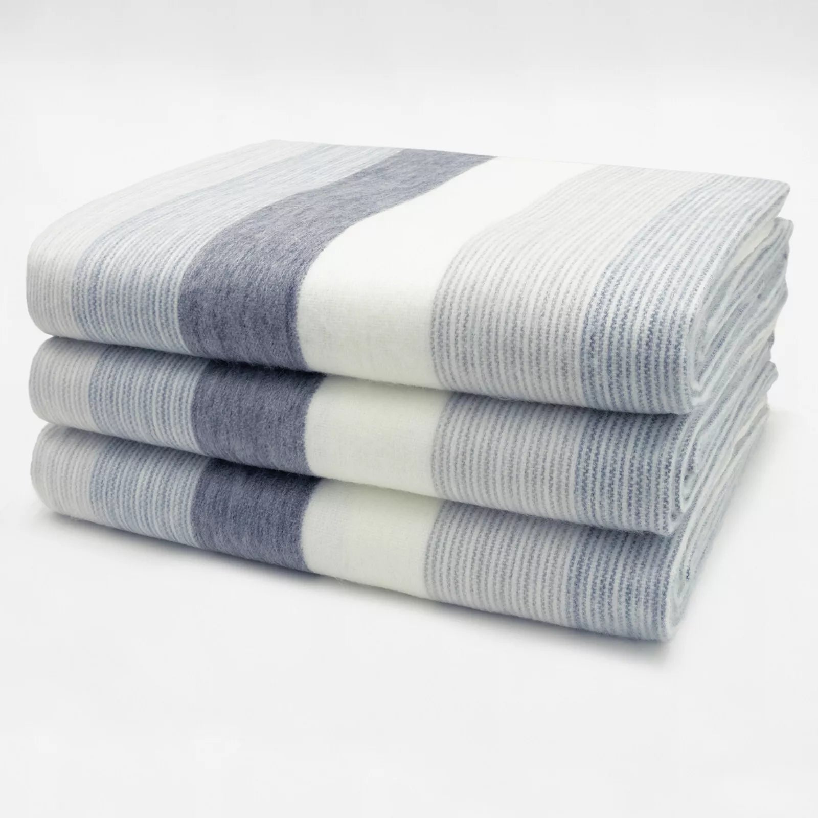 Three folded blankets display broad gray and cream stripes, stacked neatly on a plain white surface, showcasing a simple, cozy pattern in a minimalist setting.