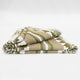 A folded blanket featuring geometric patterns in beige, green, and white rests on a plain, light surface. It has a textured appearance, suggesting it's made from woven fabric.