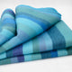Pululahua baby alpaca wool blanket – a striped, multi-colored wool blanket in shades of blue and green is neatly folded, with soft textures visible in an indoor setting