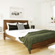A neatly made bed with striped and patterned pillows features a green blanket, set in a bright, minimalist room. A bison artwork hangs above the wooden headboard.