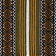 Woven textile displays geometric patterns. Vertical stripes in green, orange, white dominate the center, flanked by intricate, symmetrical diamonds and zigzags in black, brown, and white on either side.