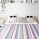 Yunga baby alpaca wool blanket – a neatly made bed with a striped blanket and decorative pillows sits in a serene room. Above, a shelf holds various decorative items, and plants add greenery to the scene