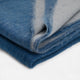 A folded, blue and gray wool blanket lies neatly on a smooth, white surface, highlighting its soft texture and subtle color variation.