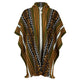A woven poncho with geometric patterns in olive green, orange, black, and white hangs against a plain background. It features vertical stripes and diamond motifs with fringe at the bottom.