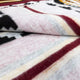 A folded wool blanket displays a Southwestern-style pattern with black, red, and yellow geometric designs. The texture appears soft and fuzzy, lying on a flat surface.