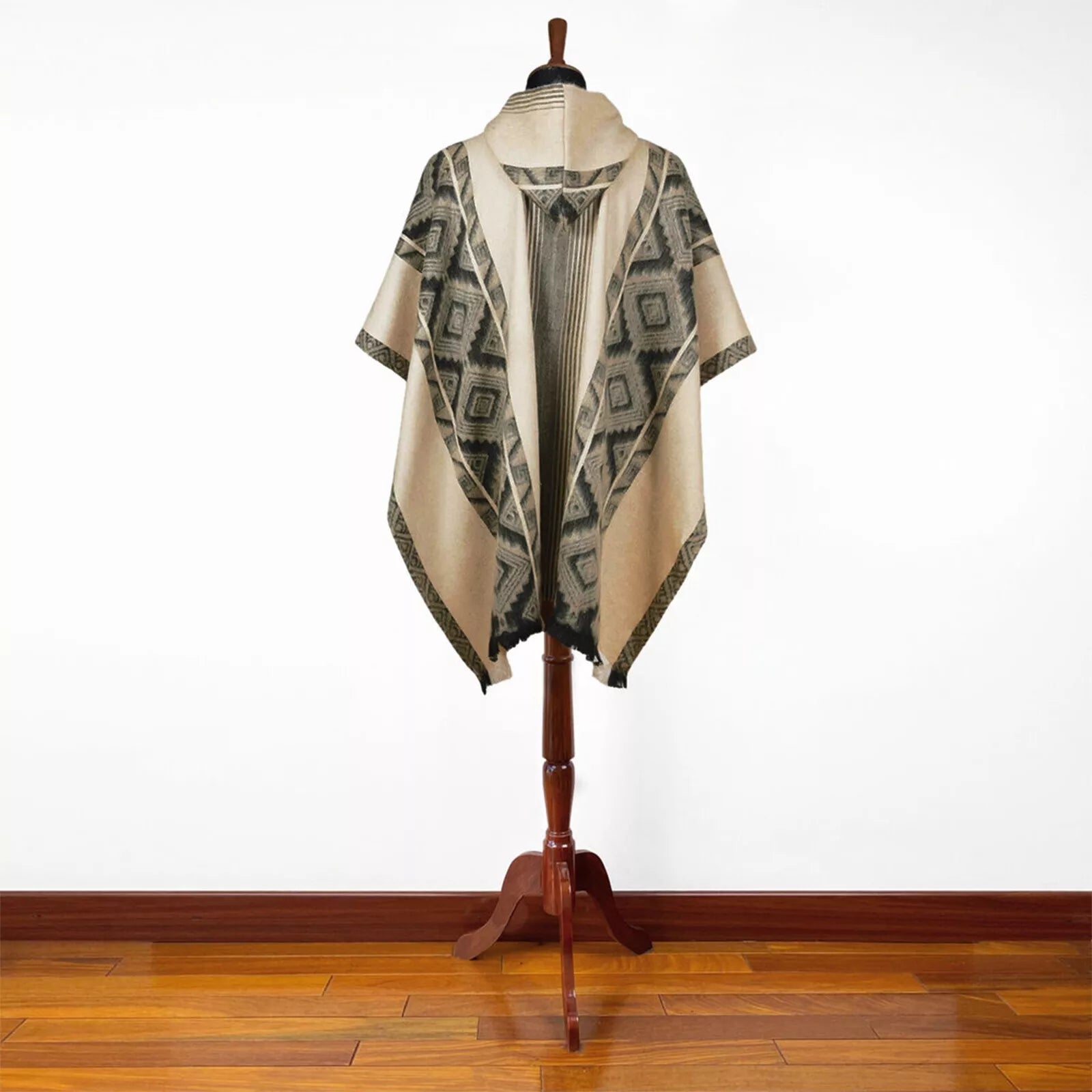 A poncho with geometric patterns hangs on a wooden stand, displayed in a room with a polished wooden floor and plain white walls.