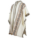 A poncho with a hood displays intricate geometric patterns in brown and black on a cream background. It features fringed edges, suggesting a traditional design, isolated on a plain backdrop.