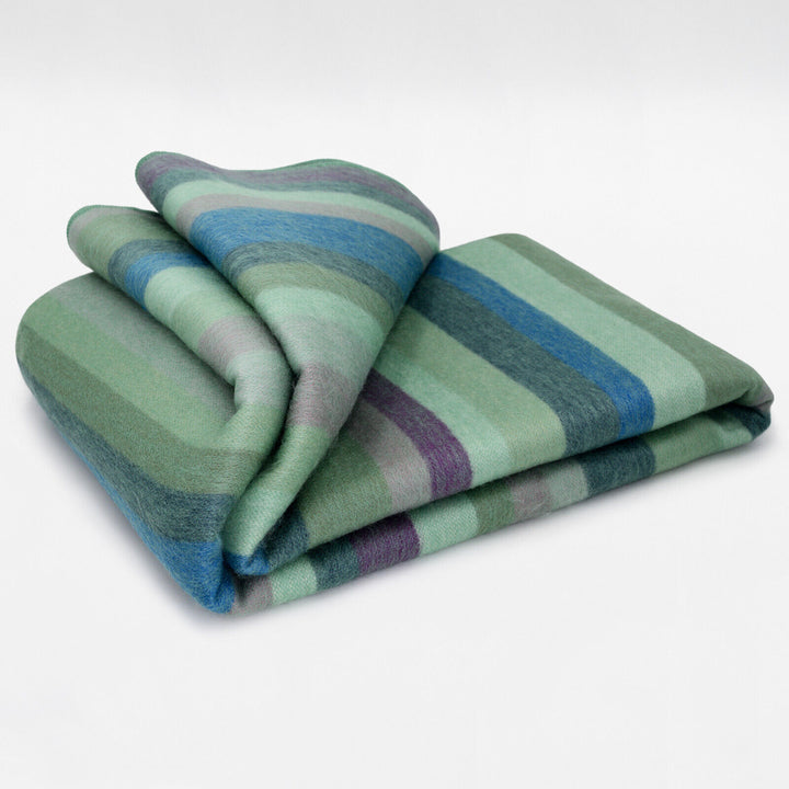 Imbabura baby alpaca wool blanket – a folded, striped blanket in shades of green, blue, and purple rests on a plain, light background, displaying its soft texture and orderly layers