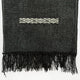 A black woven textile with fringe and an embroidered white geometric pattern in the center sits against a plain white background.