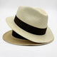 A woven straw hat with a black band rests against a plain white background, showcasing its classic, elegant design.