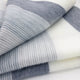 Cayambe baby alpaca wool blanket – a folded, soft fabric with alternating gray and white stripes rests on a flat surface, showcasing a smooth and textured pattern that suggests warmth and comfort