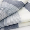 A folded, soft fabric with alternating gray and white stripes rests on a flat surface, showcasing a smooth and textured pattern that suggests warmth and comfort.