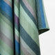 Imbabura baby alpaca wool blanket – a fabric with diagonal stripes in shades of green, blue, and purple drapes softly, suggesting a blanket or textile, set against a plain, light background