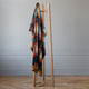 Anzu baby alpaca wool blanket – a colorful, checkered blanket hangs on a wooden clothes rack, set against a minimalistic room with light gray walls and wooden flooring