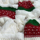 Red and green knit hats with white patterns rest on a fluffy, cream-colored fabric surface, creating a cozy, festive atmosphere.