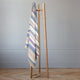 Yunga baby alpaca wool blanket – a colorful striped blanket hangs on a minimalist wooden stand, positioned in a room with pale gray walls and a light wood herringbone floor
