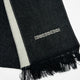 A black woven fabric with white decorative pattern features a thin white stripe and geometric designs. Black fringe borders the edge, lying flat on a white background.