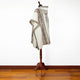 A patterned poncho drapes over a wooden mannequin stand, displayed against a plain white wall and wooden floor.
