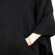 A hand wearing a red beaded bracelet is inserted into the pocket of a black textured fabric garment, with a white background.