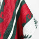 Colorful woven fabric drapes naturally, showcasing red, green, and white geometric patterns against a light background, highlighting intricate textile craftsmanship.