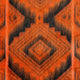 Upano kids alpaca hooded poncho – a close-up of an orange and black woven fabric displaying a geometric pattern with overlapping diamond shapes, creating a striking, symmetrical design. The texture appears soft and fuzzy