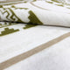 A white fabric with olive green and tan geometric patterns, partially folded, lying flat. The design includes zigzags and rectangles, giving a southwestern or tribal appearance.