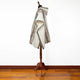 Poncho displayed on a wooden mannequin, featuring geometric patterns in beige and brown tones, set in a room with hardwood flooring and a white wall background.