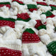 Knitted red and green hats, decorated with white patterns, are scattered on a fluffy, white fabric surface, suggesting a festive and cozy holiday setting.