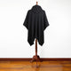 A black hooded cloak drapes over a wooden mannequin stand, displayed against a plain white wall and polished wood floor.