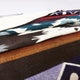 Qhusi extra large alpaca wool blanket – a folded, patterned wool blanket with geometric designs in brown, white, and teal colors lies on a flat, light-colored surface, showcasing various textures and layers