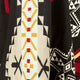A patterned fabric displays geometric designs with red, yellow, and light blue shapes on a black background, featuring symmetrical motifs and angular lines.