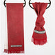 Two red scarves hang on round black hooks. One is draped flat, the other knotted, both feature white and black geometric patterns near fringed ends against a white background.