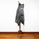 A dark gray, striped poncho is displayed on a wooden mannequin stand, set against a white wall with a hardwood floor. The poncho is draped elegantly.