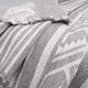 A gray and white wool blanket with geometric patterns and fringed edges drapes over a surface, showcasing its texture and design in a close-up view.
