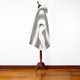 A black-and-white patterned poncho drapes over a wooden mannequin stand, situated on a polished wooden floor against a plain white wall. No text is present.
